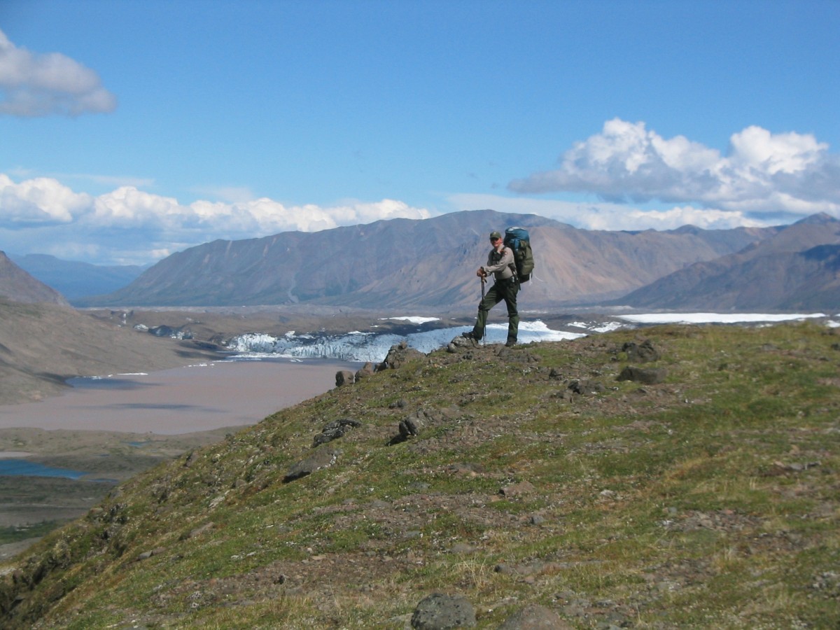 A backpacker stands in the alpine looking over the landscape in Wrangell-St. Elias National Park.